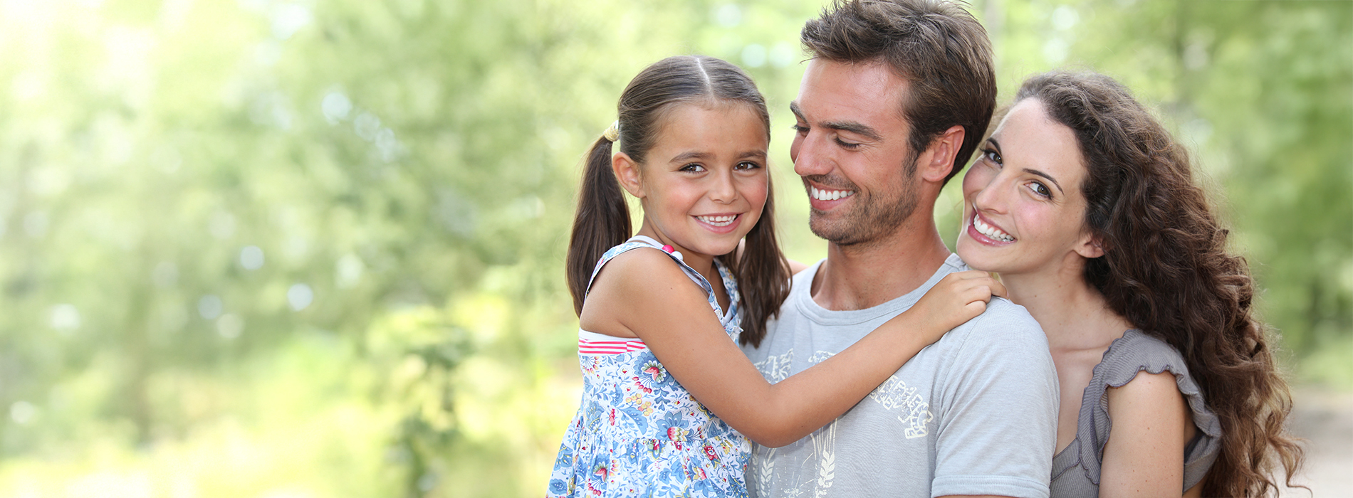 The image shows a family of four, including two adults and two children, posing for a photo outdoors on a sunny day.