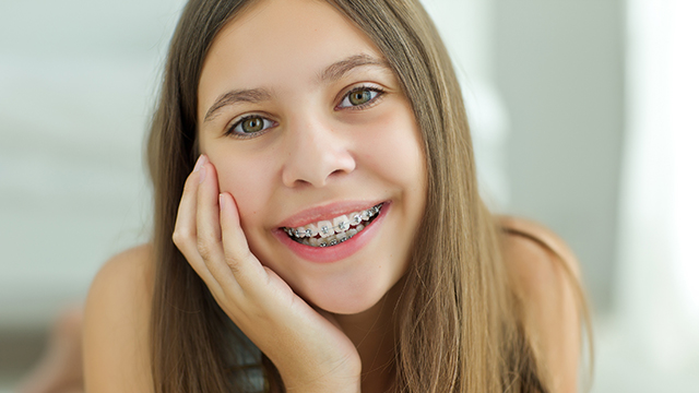 The image shows a young girl with braces smiling at the camera while posing for a portrait.